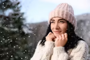 Woman with glowing skin holding her hands to her face in the winter cold.